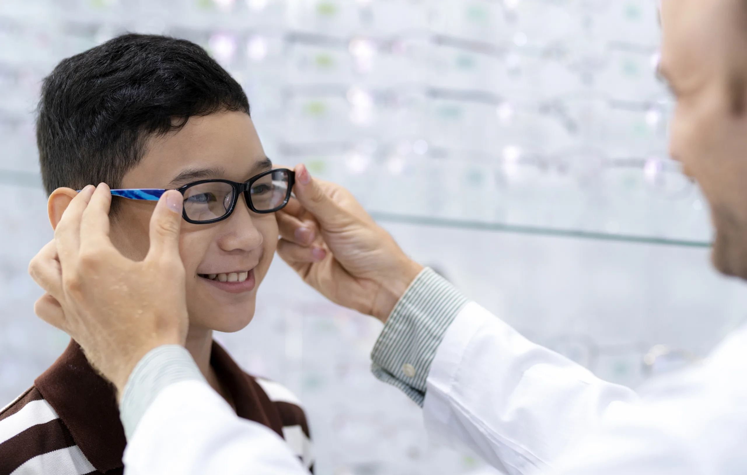 Young boy smiles has a doctor places glasses on his face